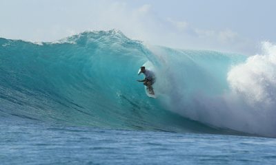 海南万宁日月湾清澈海水与整洁沙滩，冲浪者在蓝绿色海浪上驰骋，椰树成排